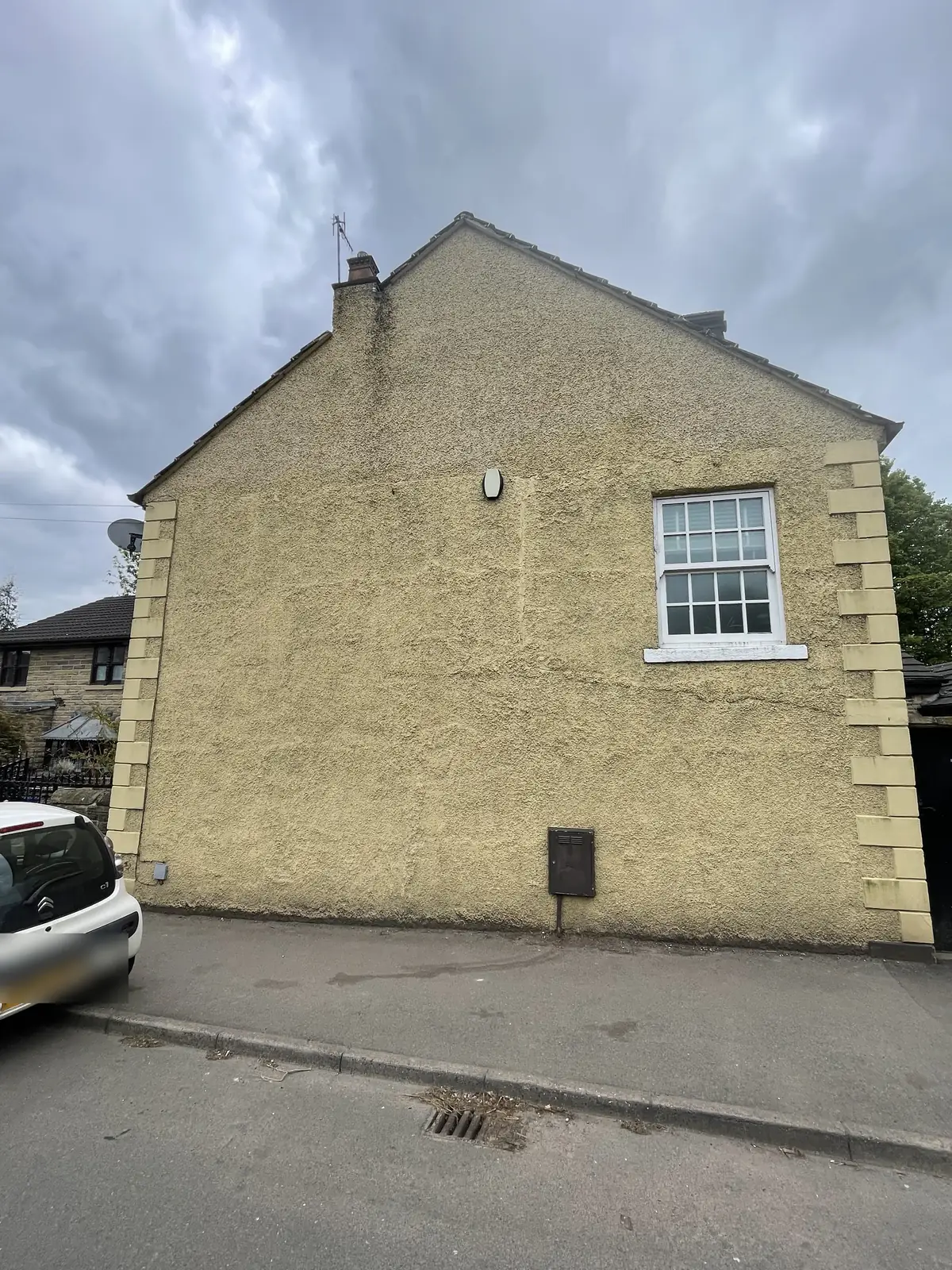 Sheffield gable end in tired buff pebbledash with stone quoins, hairline cracking visible across the wall, before rendering