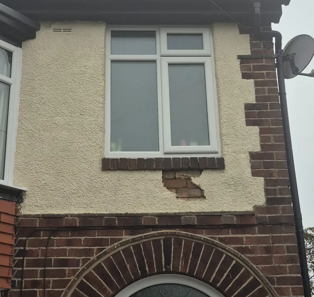 Blown render on a Sheffield house, a section fallen away below the window sill exposing the brickwork behind